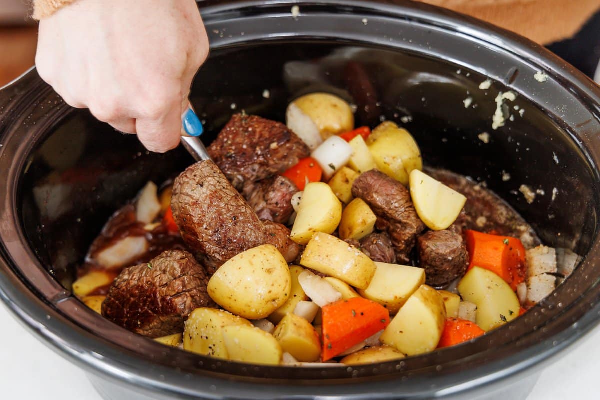 Stirring all ingredients for beef stew together in slow cooker.