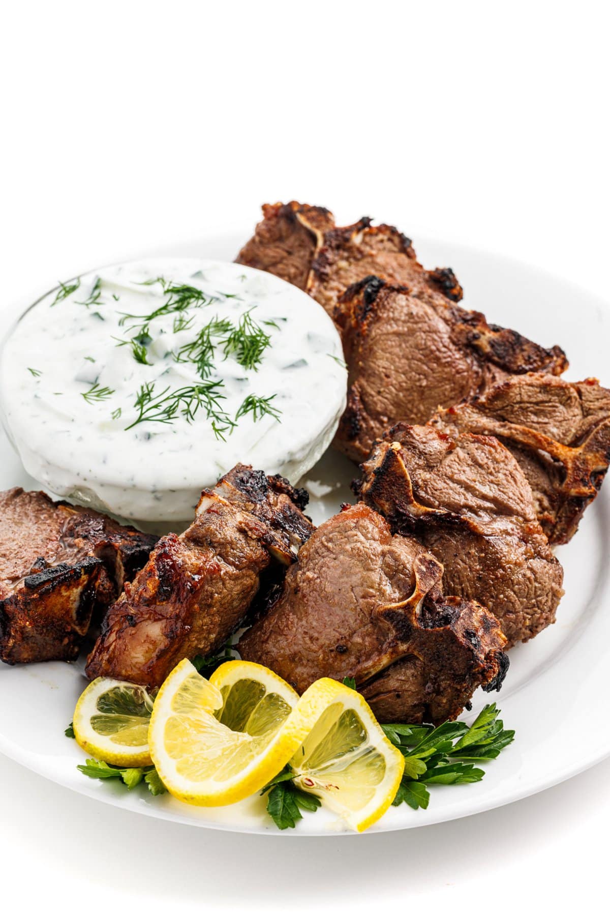 Greek lamb chops with tzatziki sauce in a small bowl next to them.