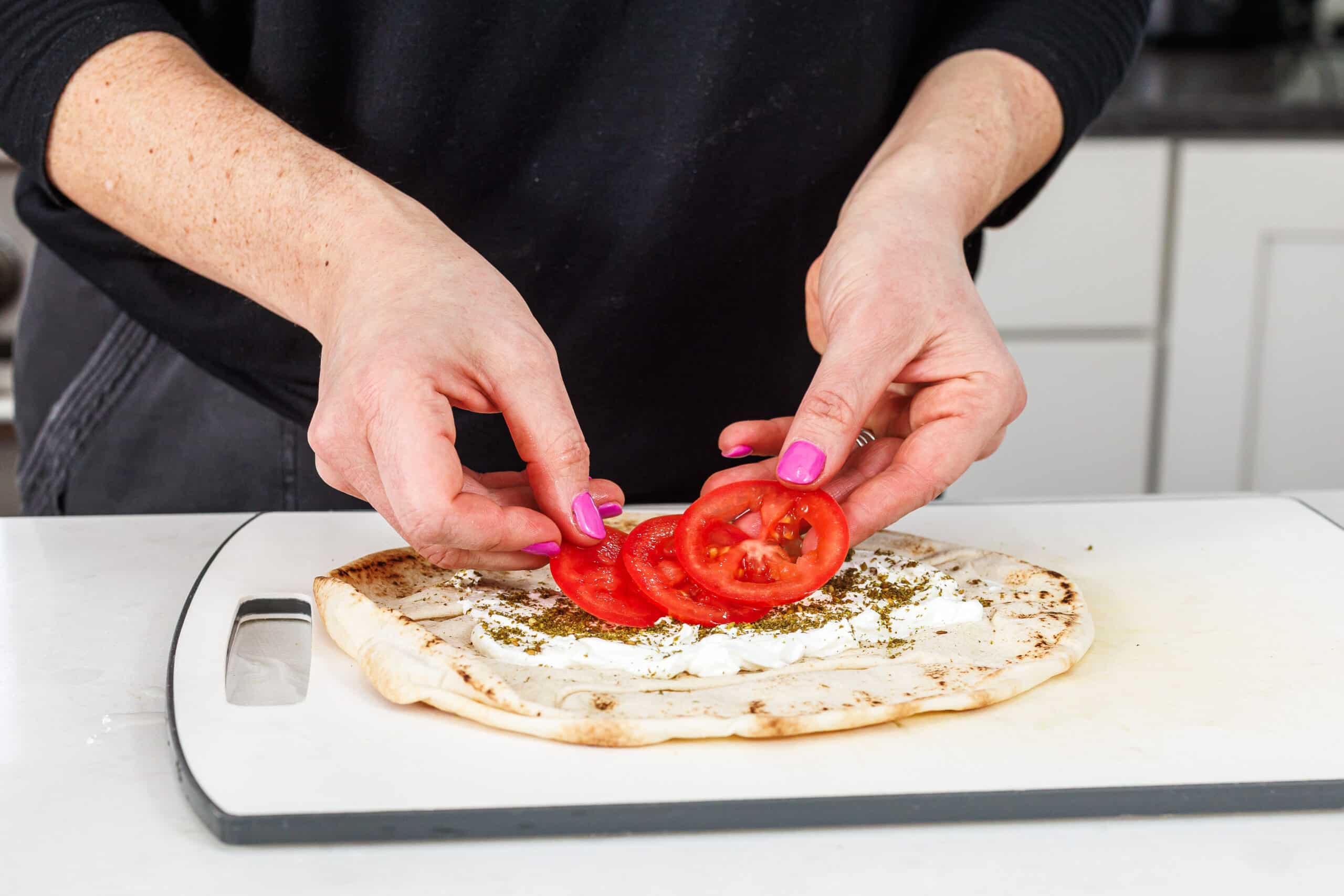 Laying sliced tomatoes on top of labneh and za'atar on pita.