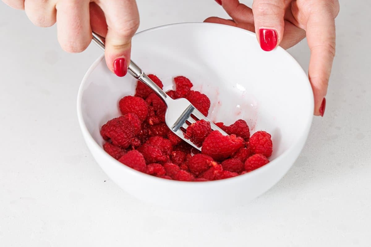 Mashing fresh raspberries with a fork in a bowl.