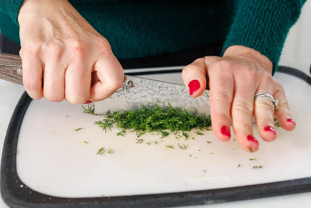 Liz mincing fresh dill on a cutting board with a sharp knife.