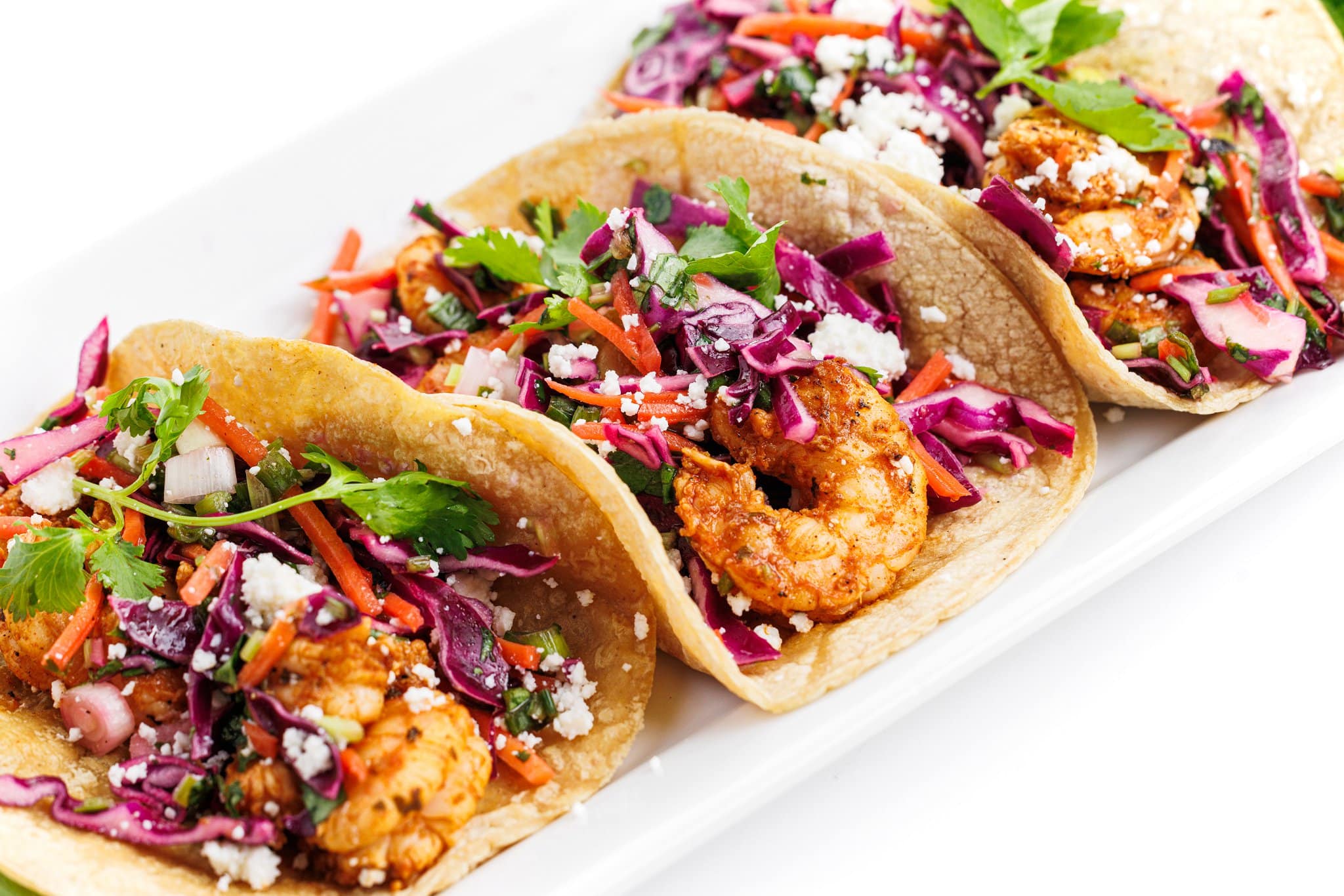 Grilled shrimp tacos with cabbage slaw and cotija cheese on a plate.
