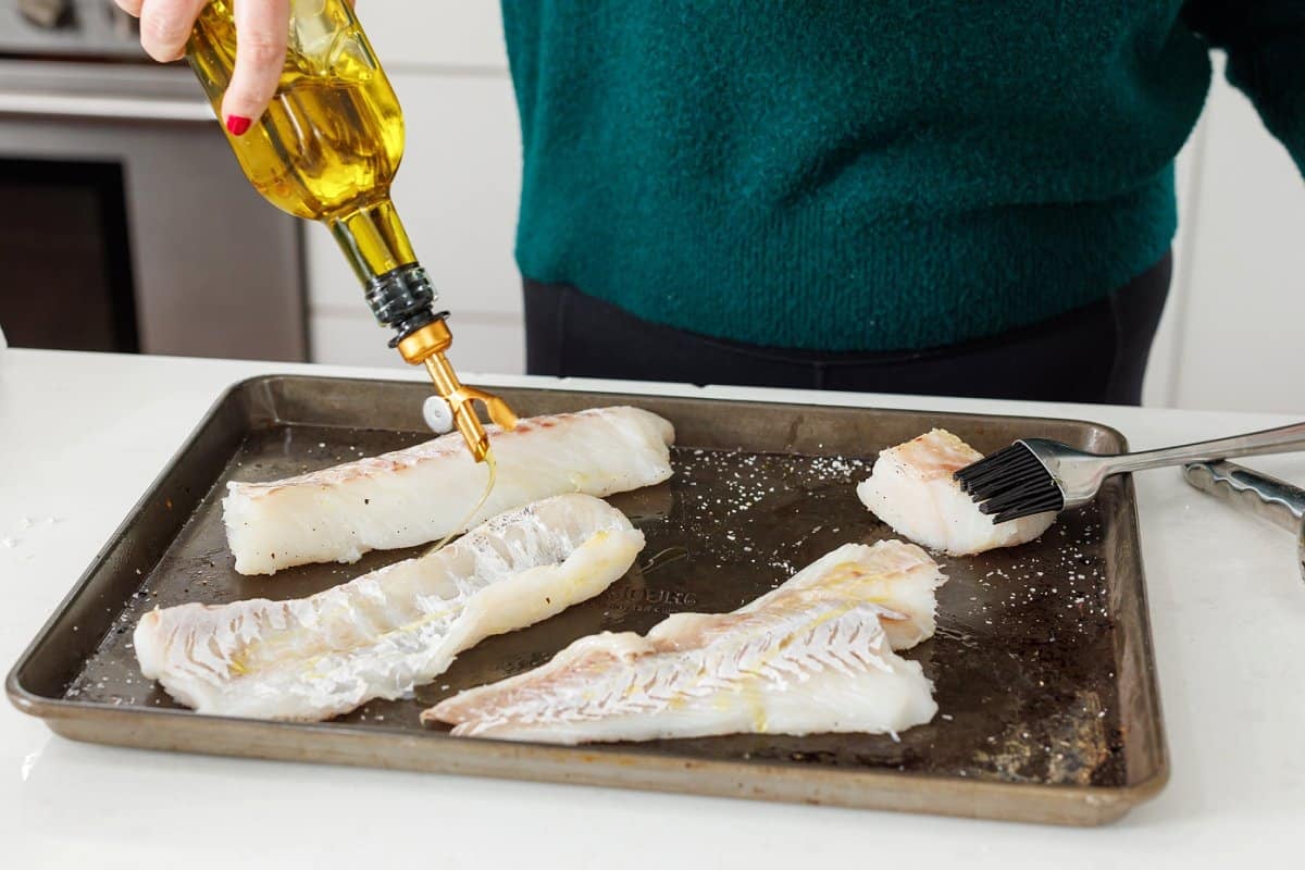 Drizzling white fish with olive oil on sheet pan.
