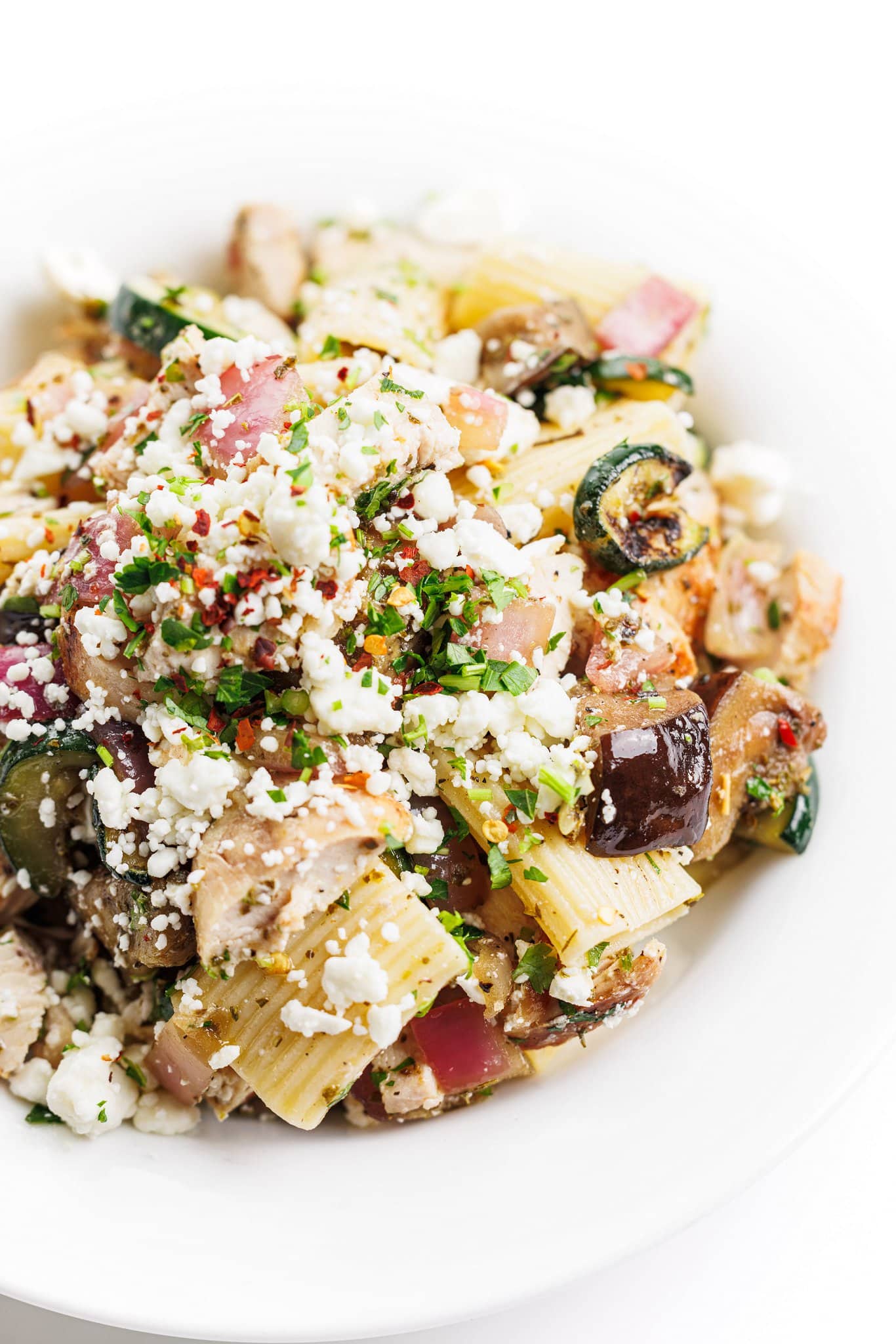 Grilled chicken and vegetable pasta salad garnished with feta and fresh herbs.