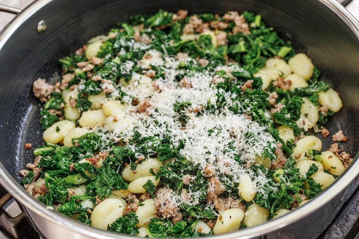 Grated parmesan cheese on top of sausage and kale gnocchi in skillet.