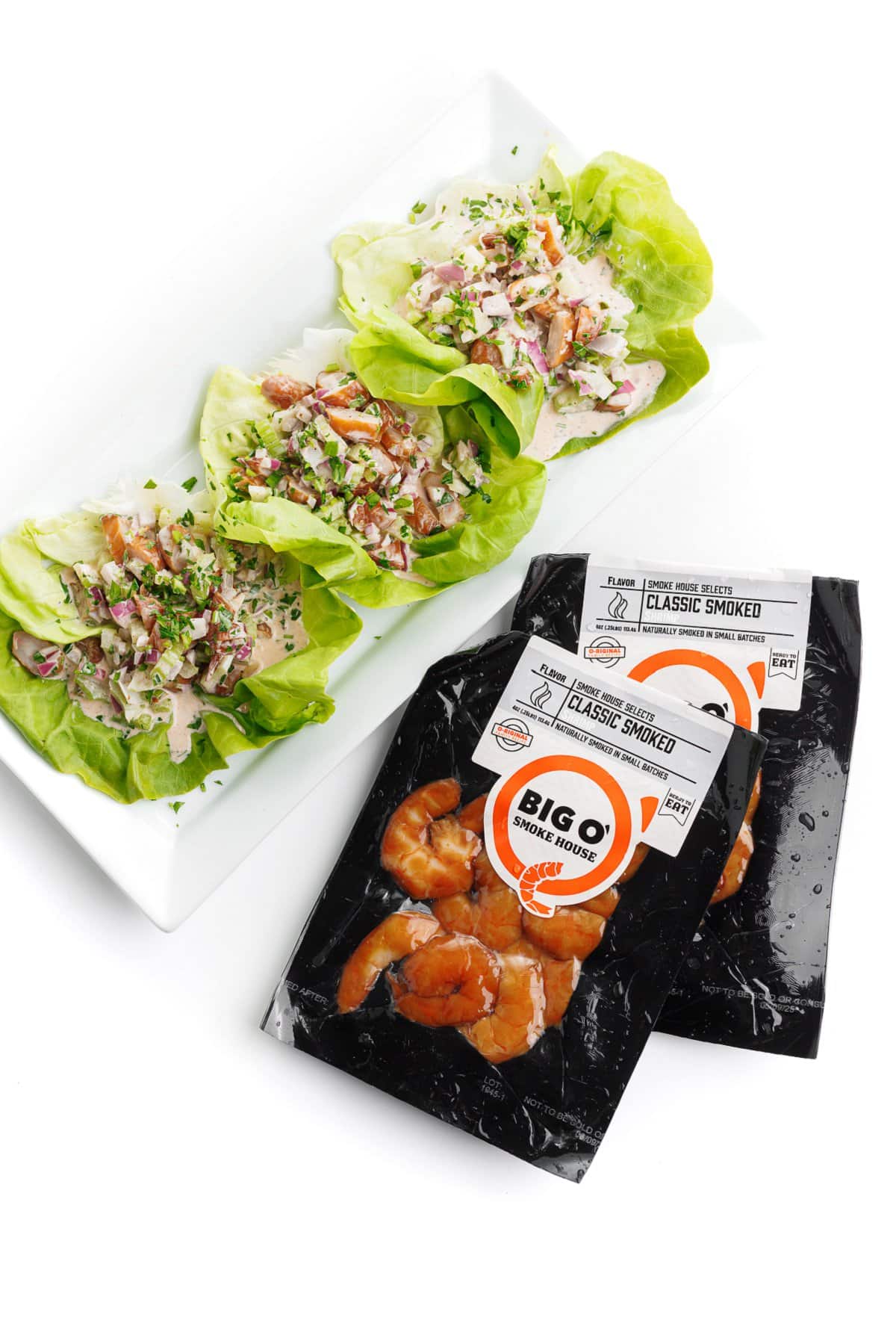 3 shrimp salad lettuce cups on a white plate next to 2 unopened packages of Big O' smoked shrimp.