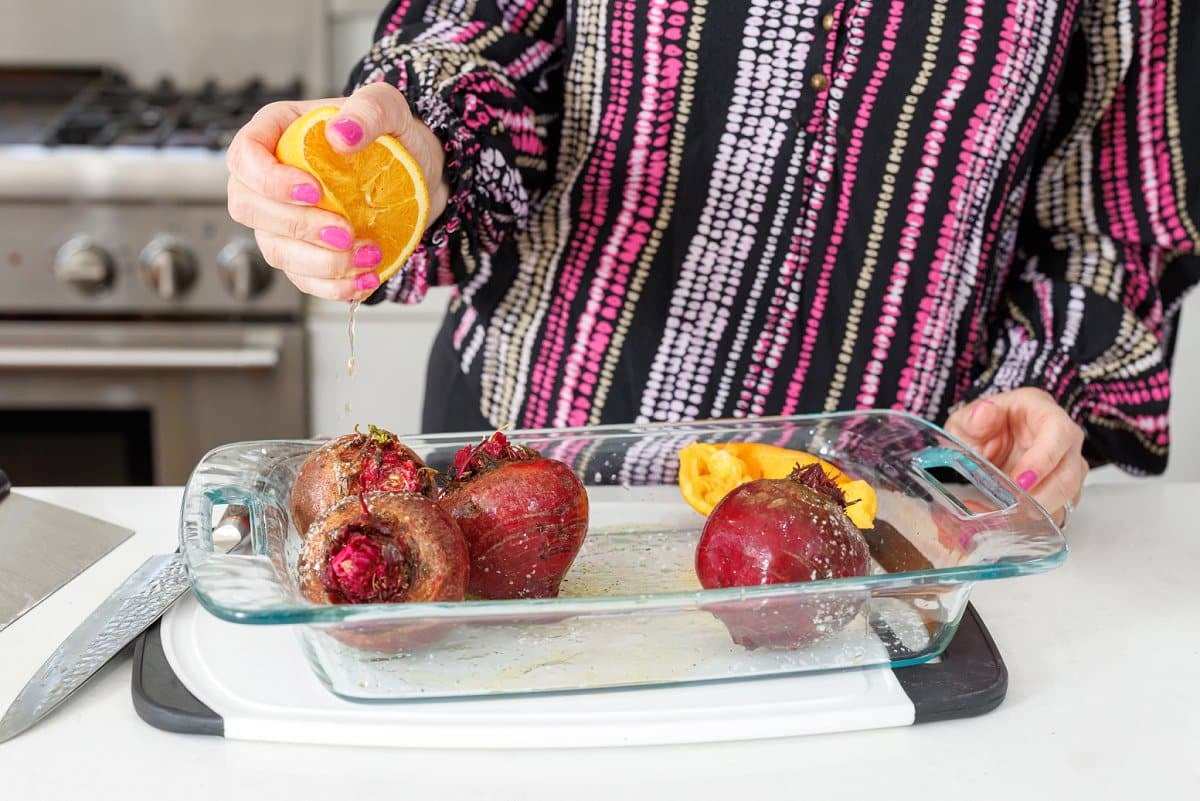 Squeezing half an orange over the top of beets in a baking dish.
