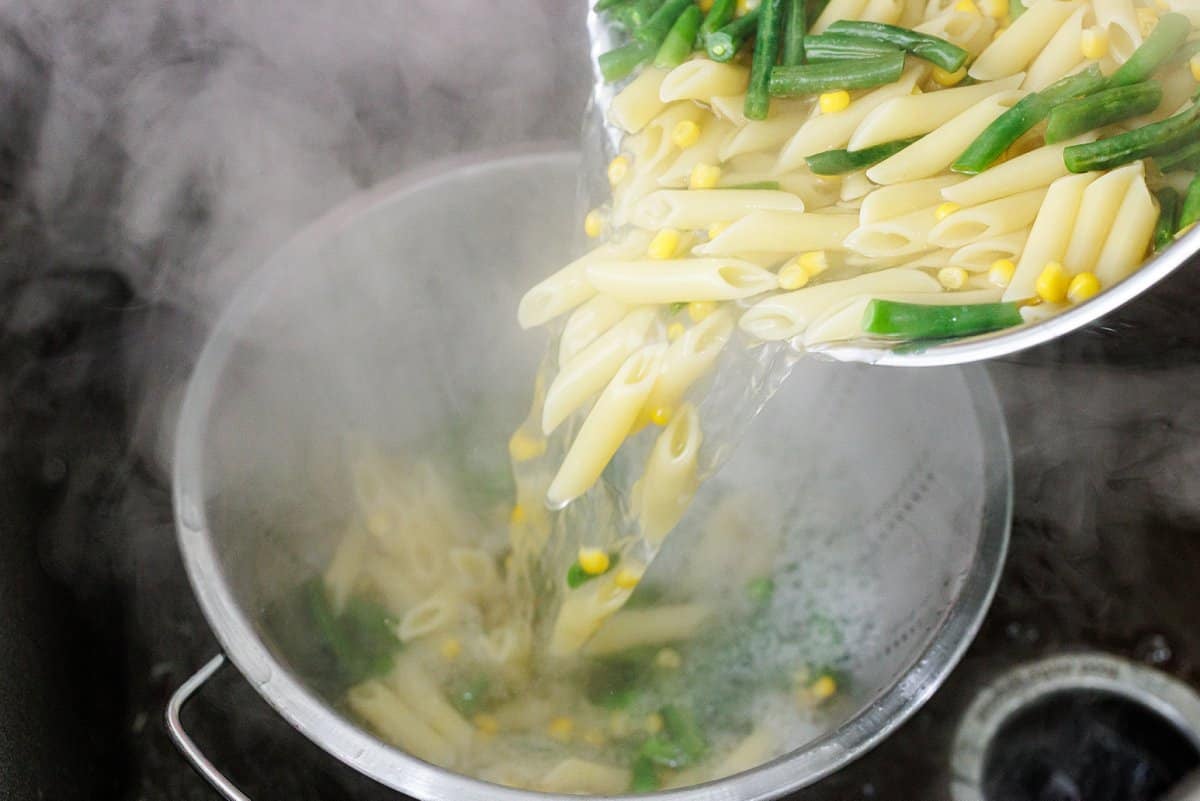 Straining pasta, green beans, and corn in a colander.