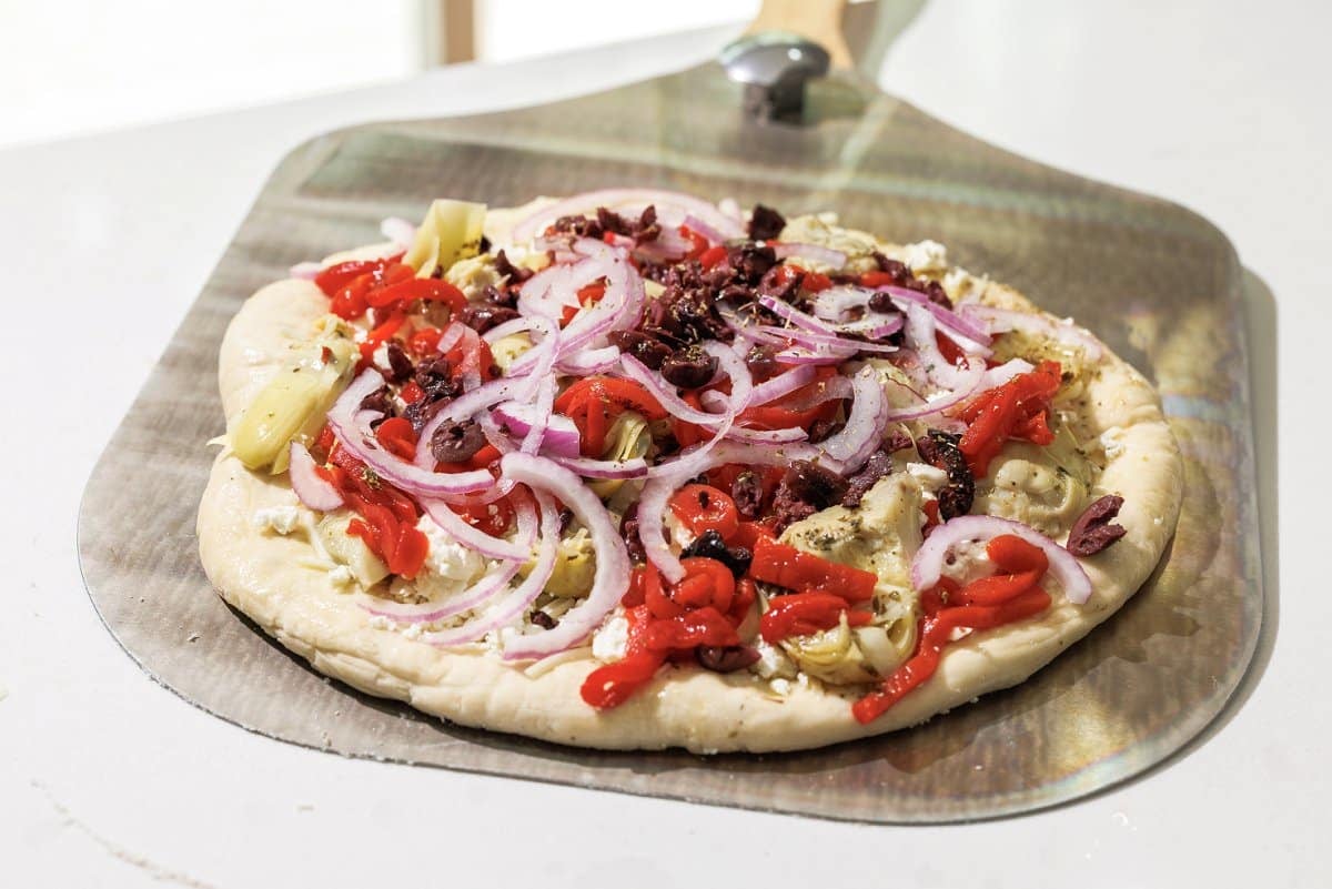 Mediterranean veggie pizza ready to go in the oven on a pizza tray.