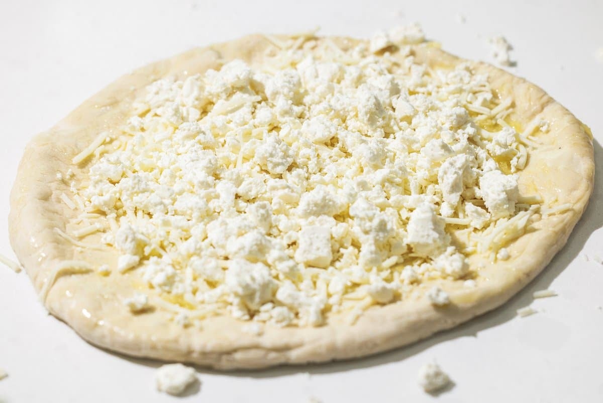 Pizza dough sprinkled with mozzarella and feta cheese.
