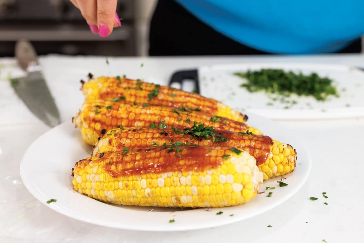 Garnishing corn with bbq sauce with fresh parsley.