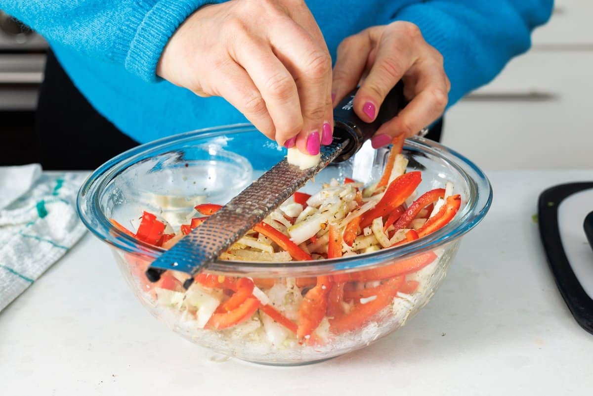 Grating garlic into a bowl of veggies with a microplane.