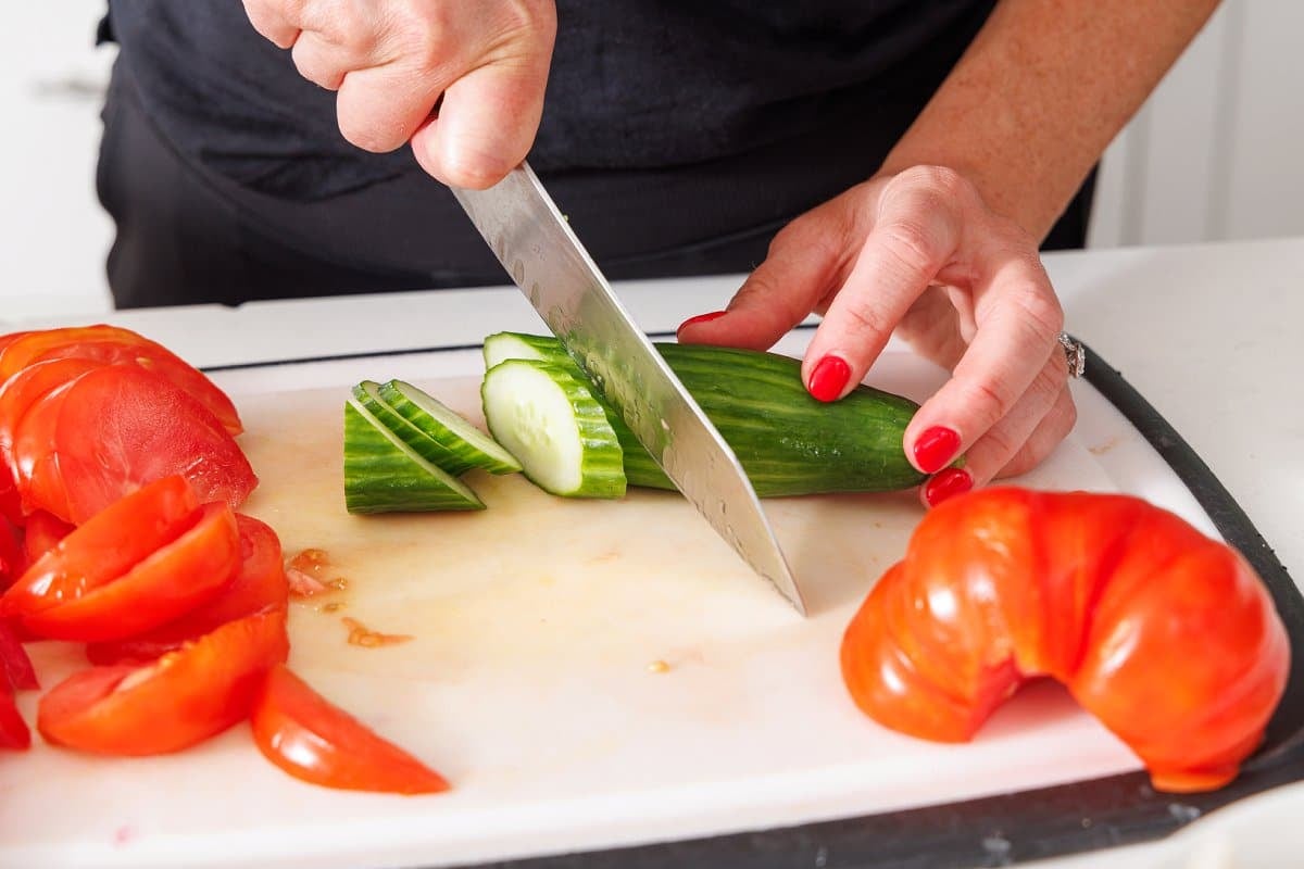 Lix slicing cucumber on a cutting board next to sliced tomatoes.