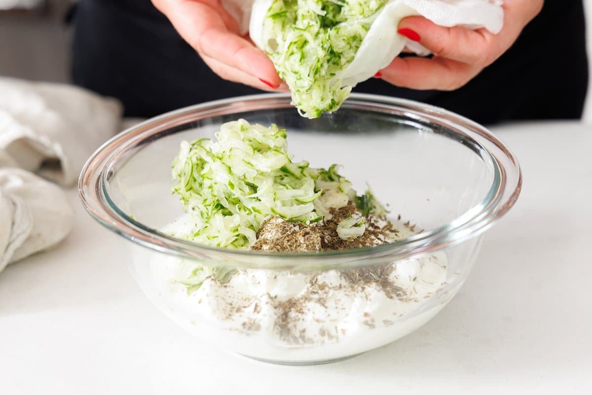 Adding grated cucumber to a bowl with yogurt and mint.
