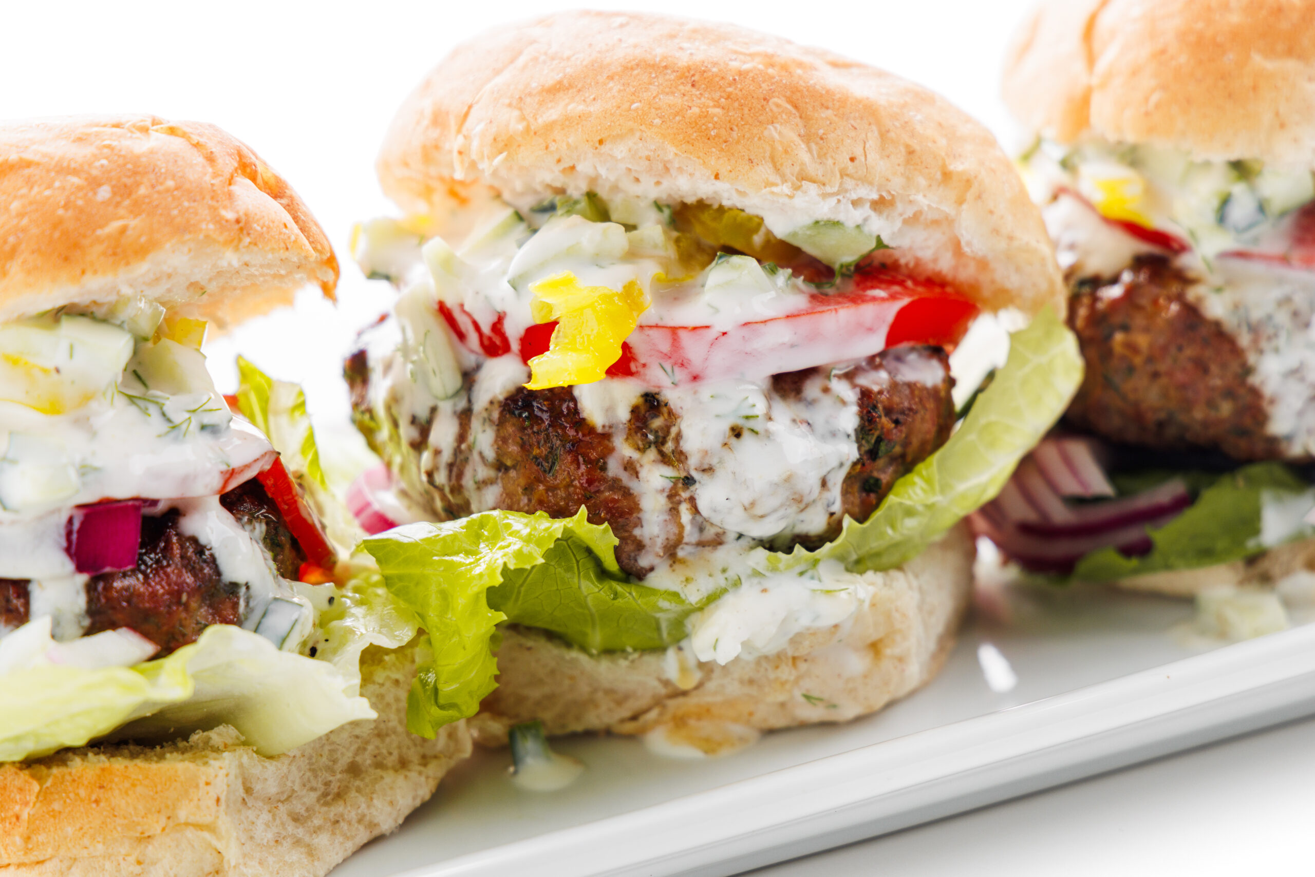 Three Greek lamb burgers with tzatziki sauce on a platter.