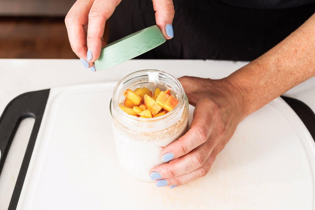 Diced peaches on top of overnight oats in a jar.