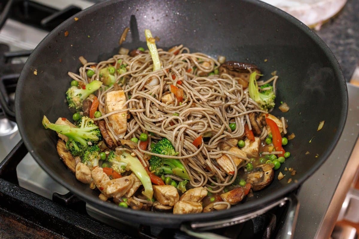 Cooked soba noodles added to wok.