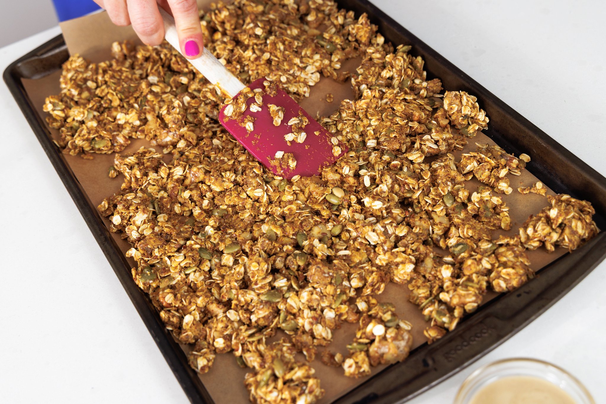 Spreading wet granola mixture on a baking sheet.