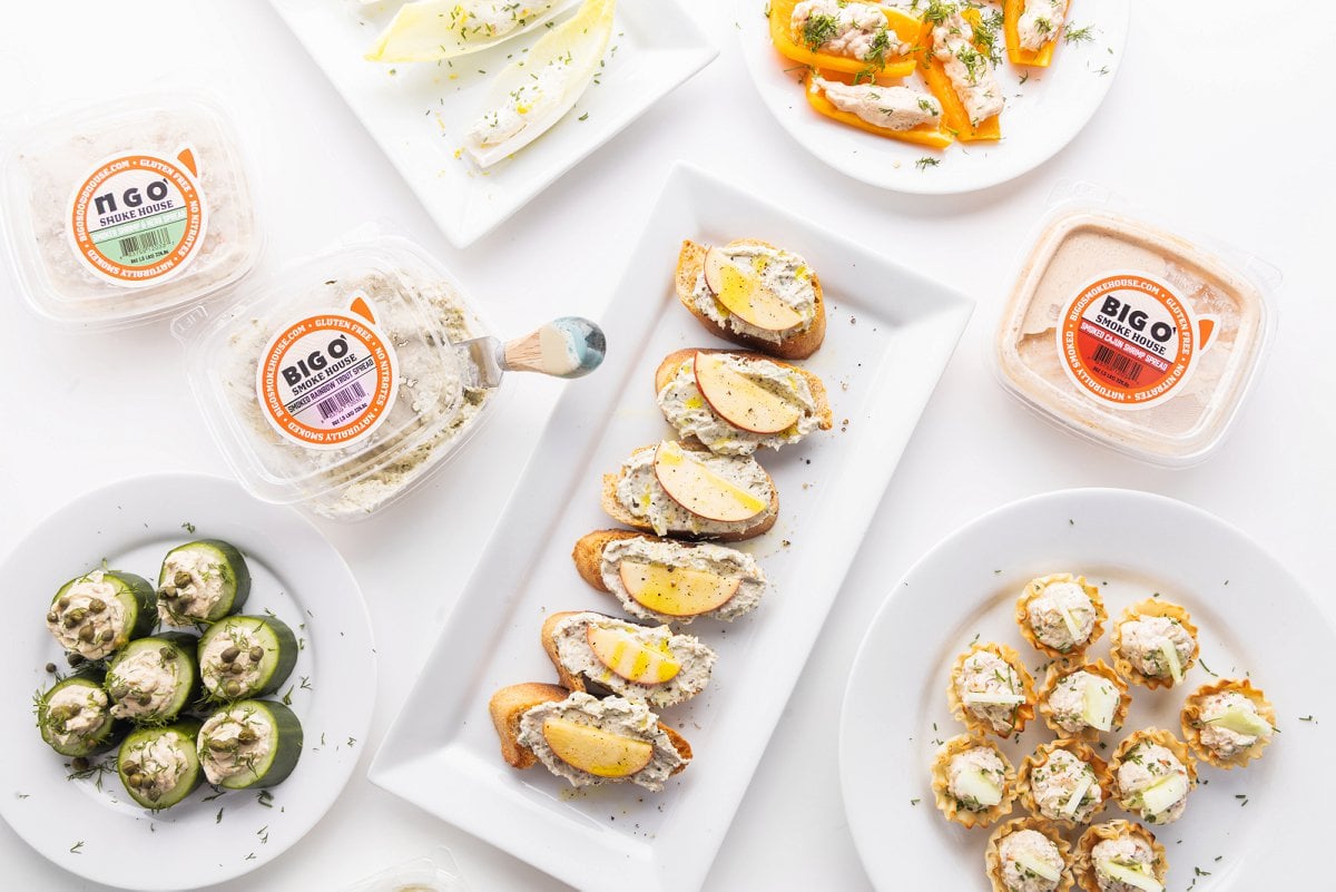 Three packages of big o' smokehouse fish dip on a counter with plates of smoked fish appetizers.