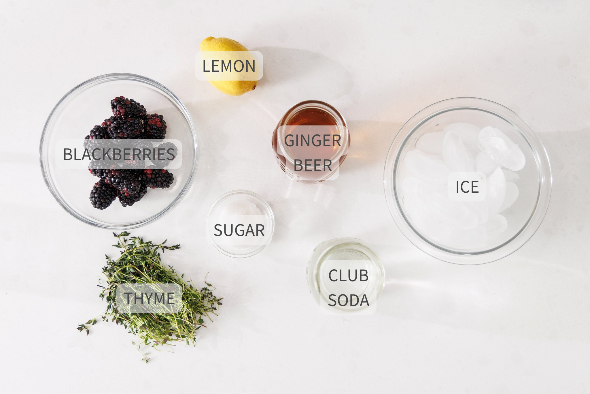 Labeled ingredients for a blackberry ginger smash mocktail on a white counter.