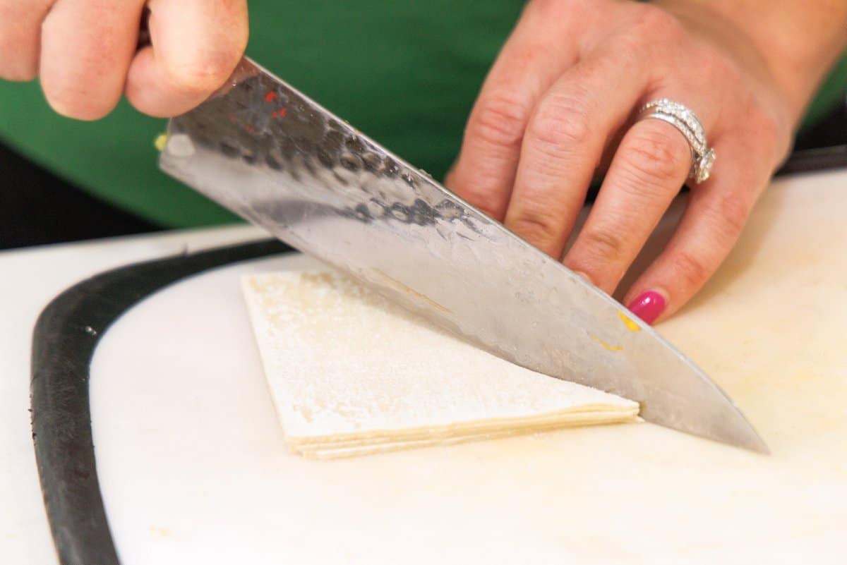 Using a sharp knife to cut wonton wrapper dough into triangles.