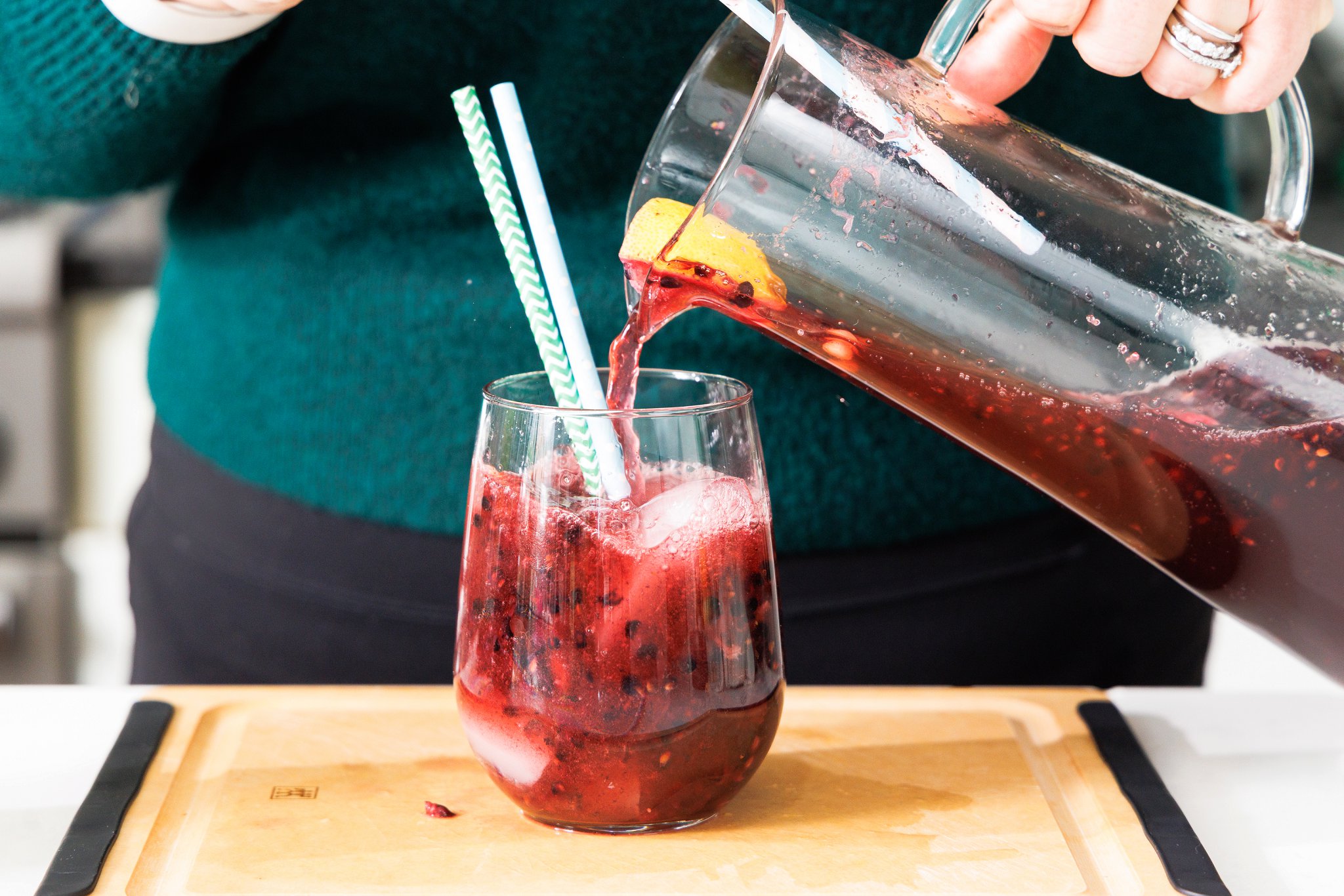 Pouring blackberry ginger smash from a pitcher into a stemless wine glass.