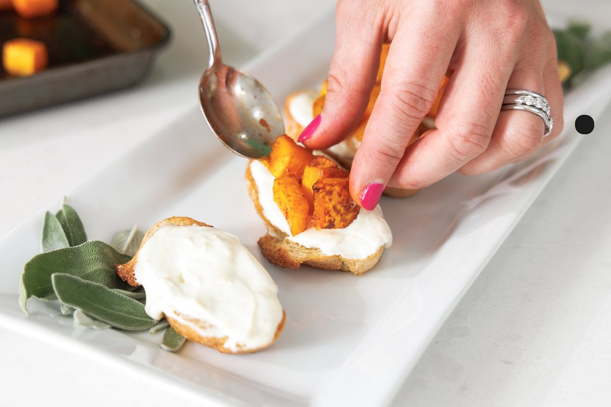 Putting roasted butternut squash on top of goat cheese spread on crostini.