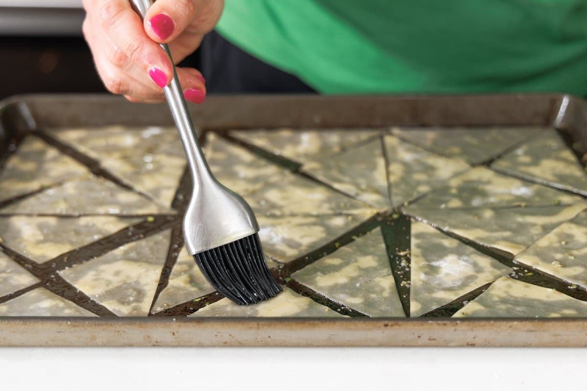 Brushing wonton wrapper dough with olive oil on a baking sheet.