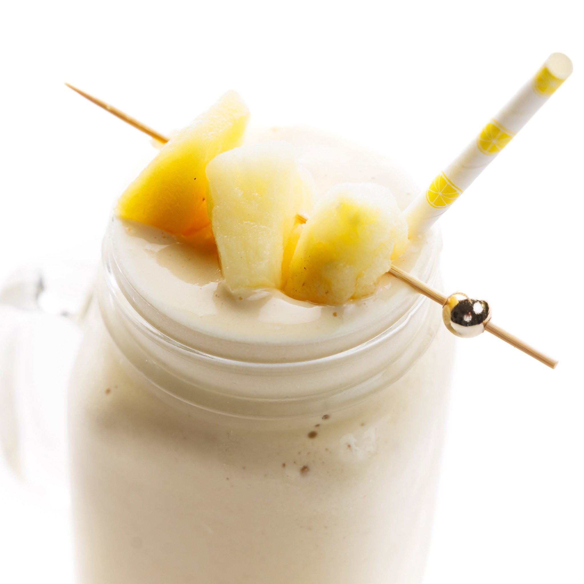 Pina colada protein smoothie topped with fresh pineapple on a toothpick and a yellow stiped straw.