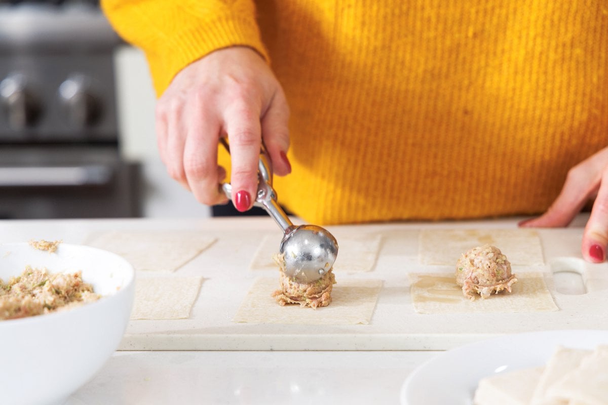 Using cookie scoop to put pork filling in the center of a wonton wrapper.