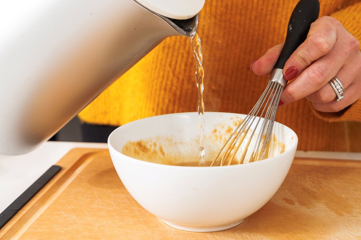 Pouring hot water into a bowl with the peanut sauce.