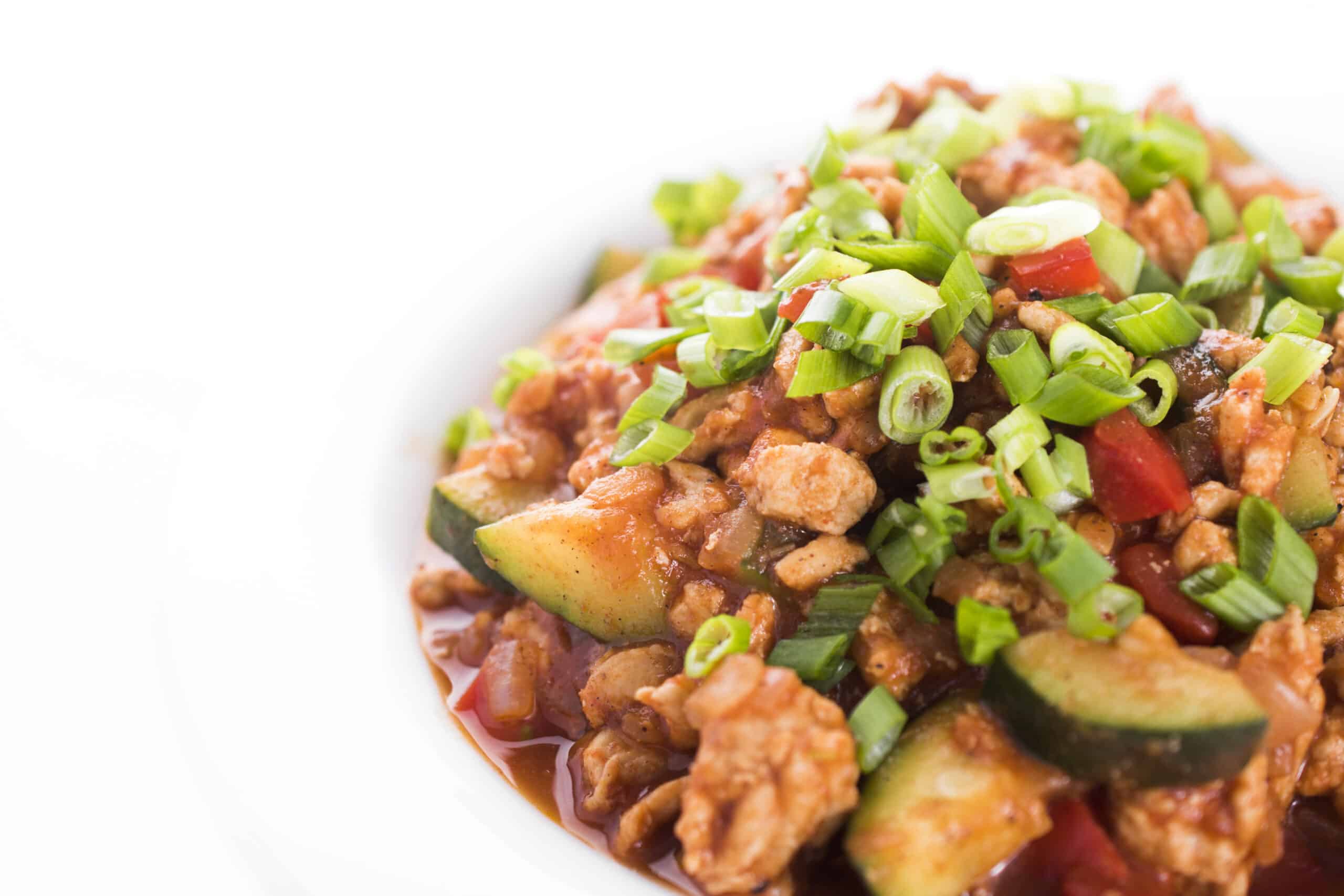 Ground turkey and zucchini with Indian spices in a bowl topped with fresh green onions.