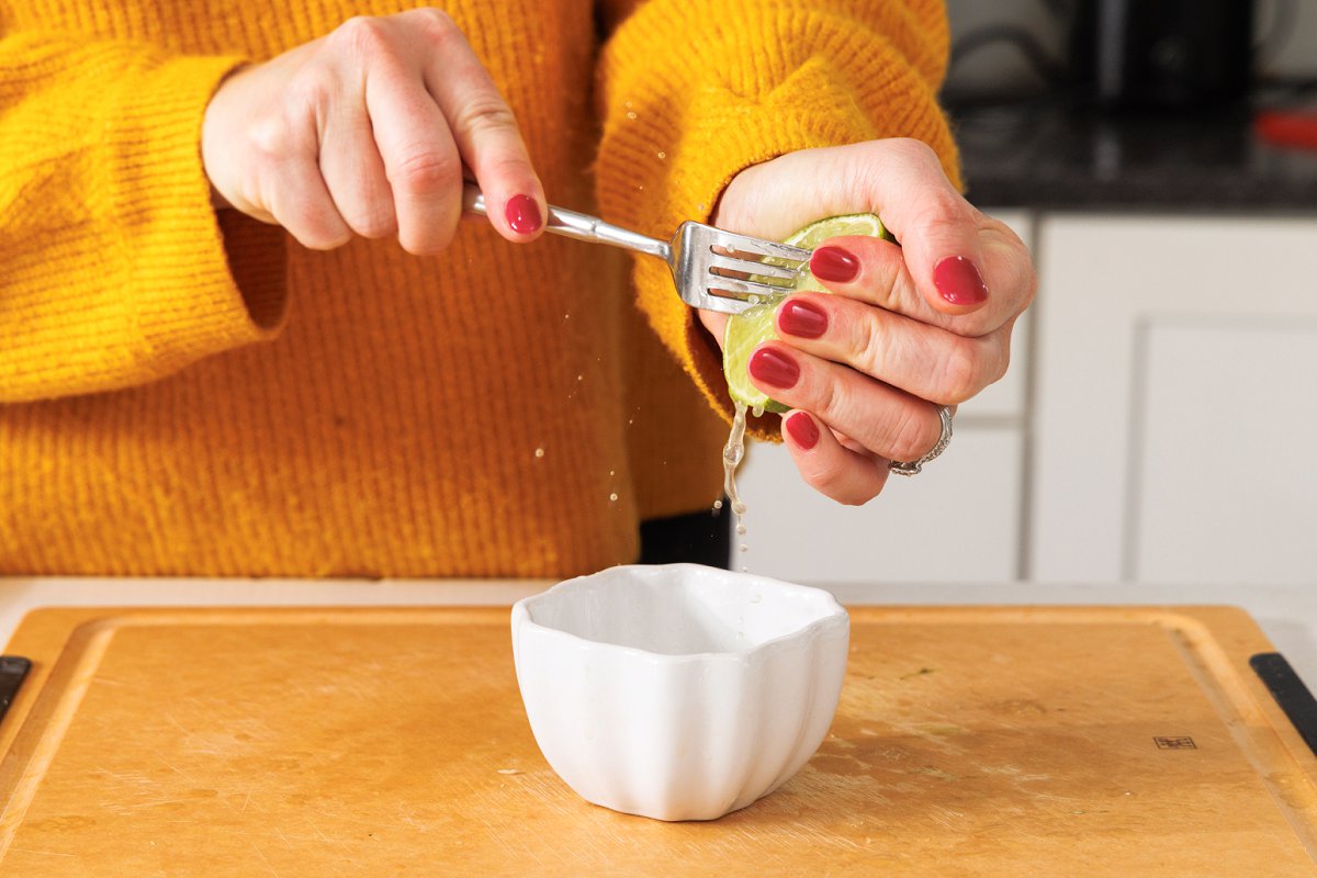 Using a fork to juice lime into a small white bowl.