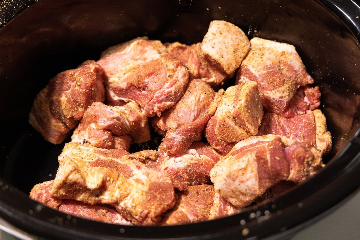 Seasoned pork roast chunks in slow cooker pot.