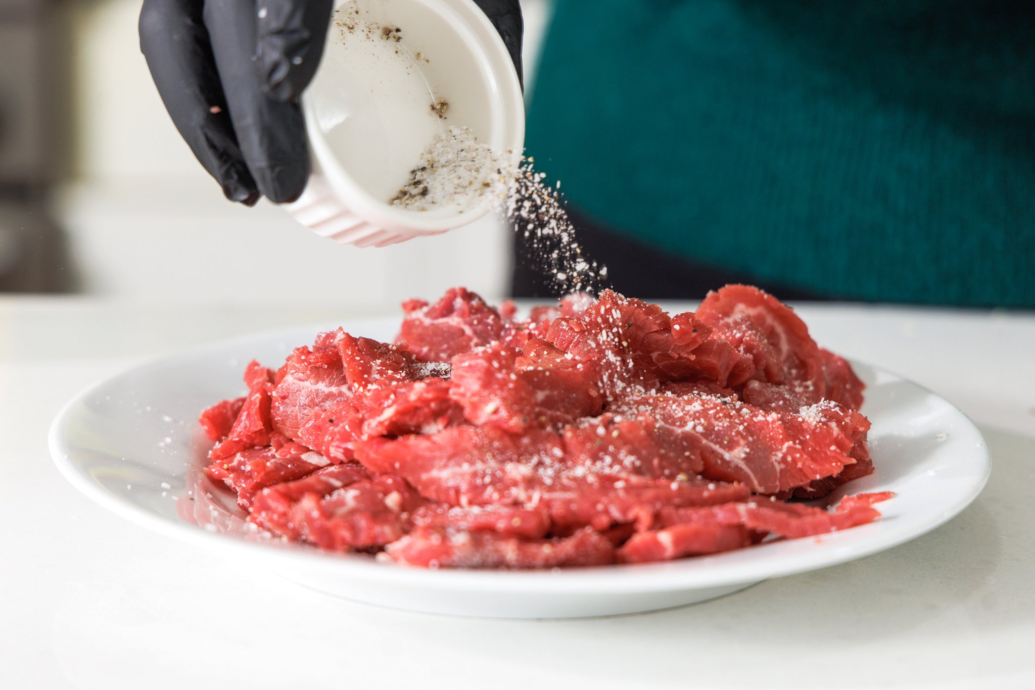 Sprinkling sliced beef strips with salt and pepper.