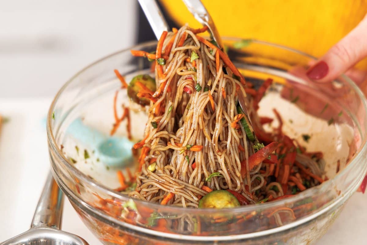 Tossing rice noodles, shrimp, and veggies in vinaigrette in a large bowl.